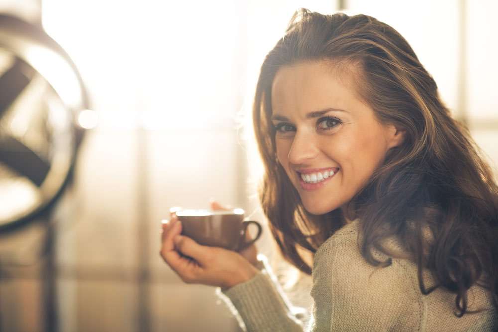 Portrait of happy young woman with cup of hot beverage